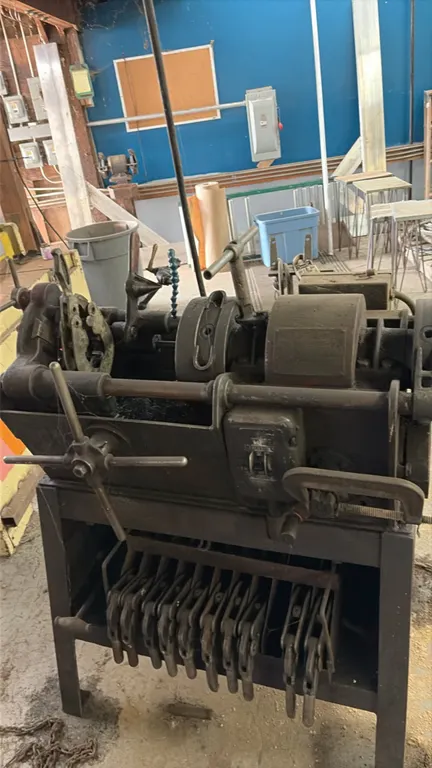 Stationary pipe threading machine. Features an integrated metal cabinet stand with built-in die storage rack holding assorted die heads, front hand wh