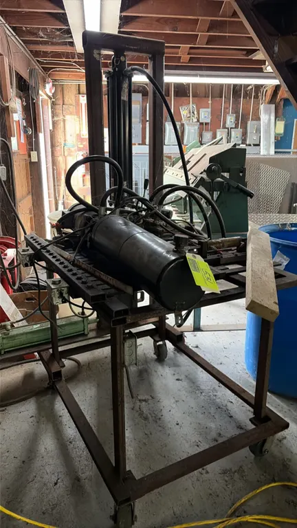 Hydraulic shop press mounted on a rolling steel work table. Features vertical hydraulic cylinder assembly, hydraulic pump and reservoir unit, manual v