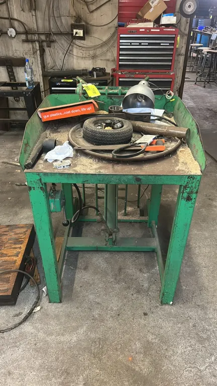 Hydraulic metal work table. Features fabricated steel construction with raised side containment lips, integrated hydraulic cylinder mechanism, and hyd