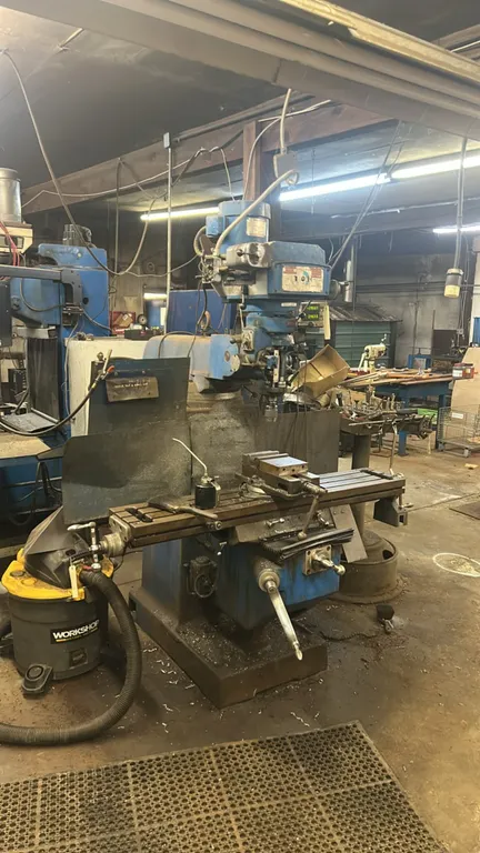 Vertical knee-type turret milling machine. Features swivel milling vise, 2-axis digital readout (DRO), variable speed head, drill chuck, and manual cr