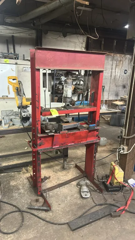 H-frame hydraulic shop press. Features a top-mounted hydraulic ram with integrated pressure gauge, return springs, and an adjustable height bed. Mount