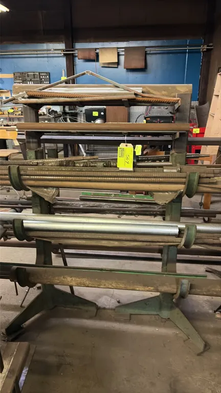 Green metal multi-tier cantilever bar stock and pipe storage rack. Includes assorted threaded rod, pipe, and bar stock contents.
