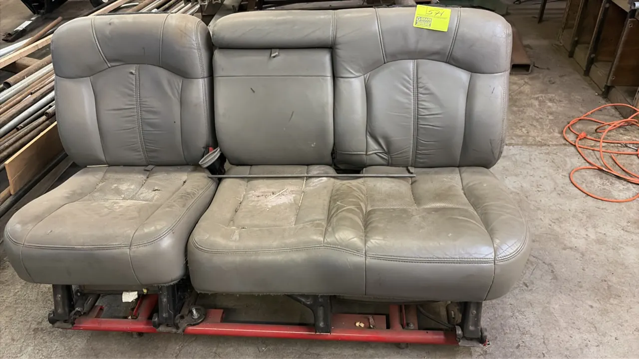 Portable split bench seat. Features gray upholstery with fold-down center console armrest. Mounted on a red metal frame base. Note: Upholstery has hea