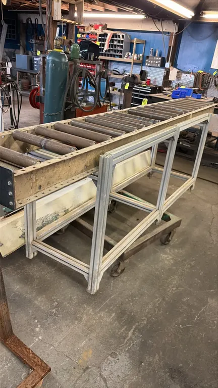 Metal roller conveyor. Features steel rollers, end stop plate, and an aluminum extrusion support stand. 10'L.