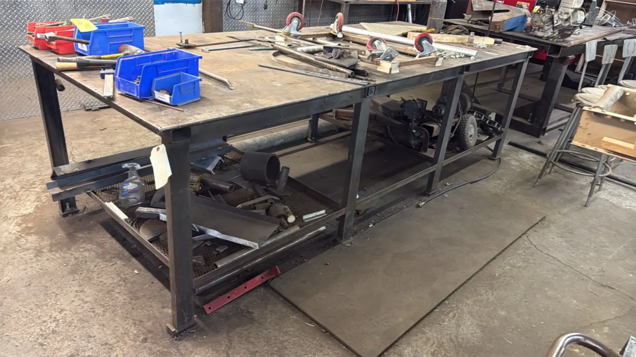 Steel work table. Features solid steel plate top and lower expanded metal storage shelf. 10'L x 49"W. Includes assorted loose contents on and below ta