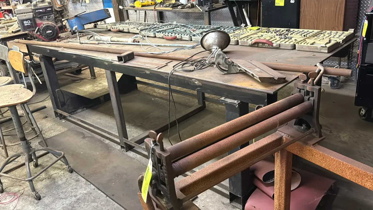 Metal work table. Features a steel plate top and welded steel frame construction with bottom support rails. 10' x 49". Contents not included.