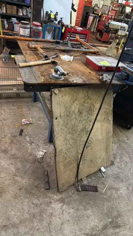 Metal work table. Features a heavy-duty steel plate top and a welded square-tube steel frame. 52" x 55". Contents and tabletop tools not included.