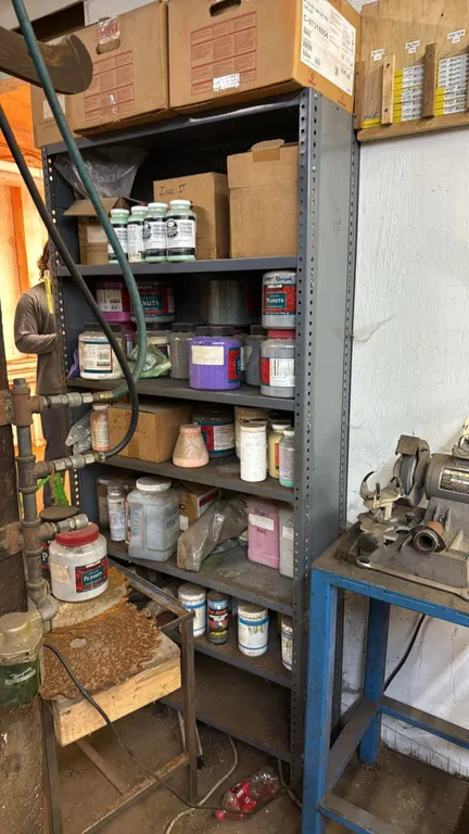 Metal storage shelving rack with powder coating and paint supplies. Features multi-tier steel shelf construction. Includes assorted powder coating pow