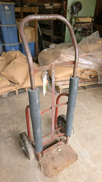 Metal hand truck. Features steel tubular frame construction with continuous loop handle, foam-padded upright sleeves, and solid rubber wheels.