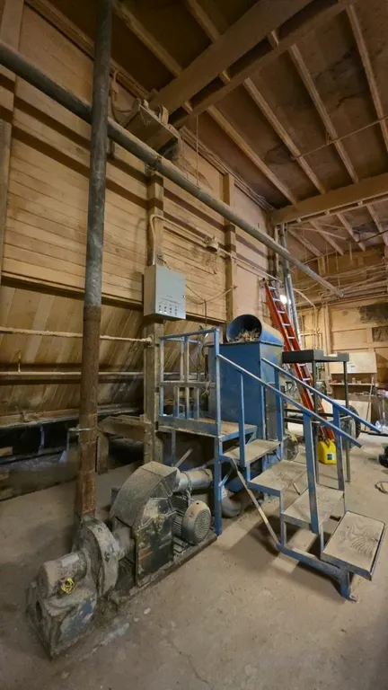 Industrial wood chipper. Features top feed hopper, poly barrel feed stand, elevated platform with access stairs, discharge blower assembly, and contro