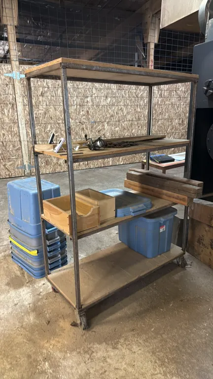 4'L 4-tier mobile metal storage rack. Features four wood shelves and welded steel frame. Mounted on casters. Includes assorted contents as shown.