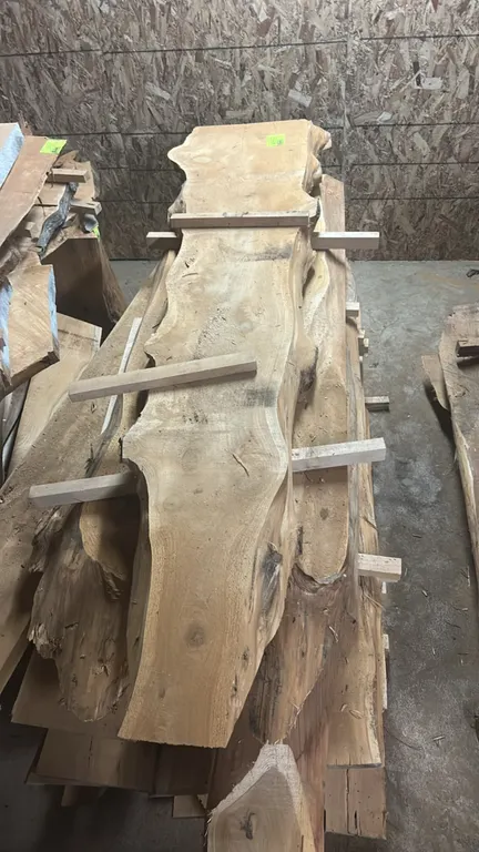 Live edge cedar boards. Features stacked natural live edge wood slabs separated by wooden spacers. Dimensions: 103"L x 24"W x 43"H.