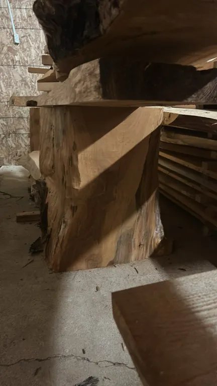 Live edge cedar tree stumps. Features natural cedar wood grain with live edge details. Dimensions: 13" x 16" x 29". Slabs and lumber resting on top no