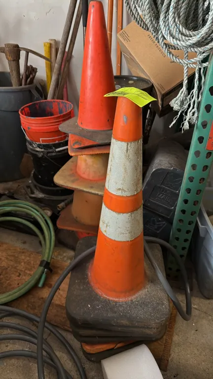 Orange safety cones. Features weighted black rubber bases and reflective collar striping. Background items and surrounding equipment not included.