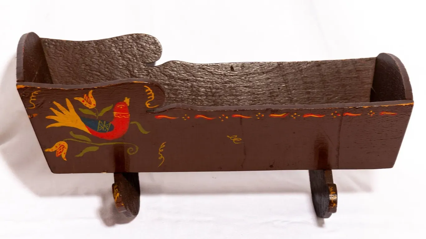 FOLK ART PAINTED DOLL CRADLE IN BROWN WITH FLORAL AND BIRD MOTIFS.