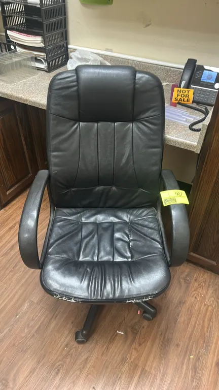 Cushioned executive office chair. Features black upholstered high back and seat with fixed armrests. Mounted on a 5-star swivel base with casters. Not