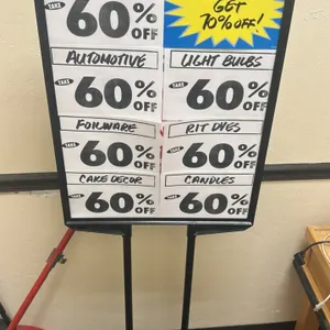Metal floor sign stand. Features a black finish, dual upright support posts, and framed sign holder. 2'W. Mounted on a flat rectangular metal base.