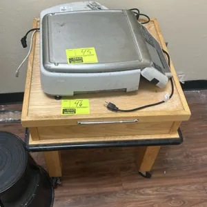 Wooden mobile table. Features raised edge trim on tabletop, bumper guard perimeter, and front pull handle. 2'L. Mounted on swivel casters. Scale and b
