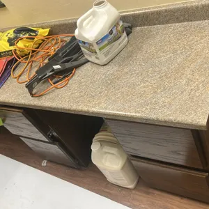 L-shaped laminate countertop with base and wall cabinets. Features speckled faux-stone laminate countertop with integrated backsplash, woodgrain finis