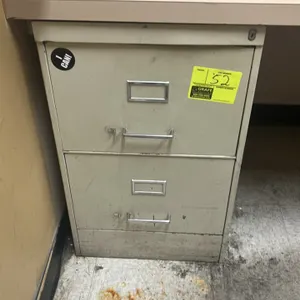 Metal 2-drawer vertical filing cabinet. Features pull handles, integrated label holders, and top lock cylinder. Desk and surrounding contents not incl