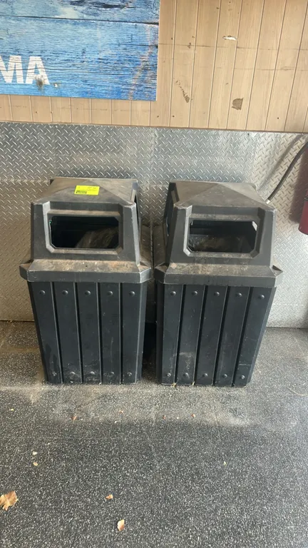 Polyethylene trash receptacles. Features black molded plastic construction, slat-style paneled design, and canopy lids with disposal openings. Content