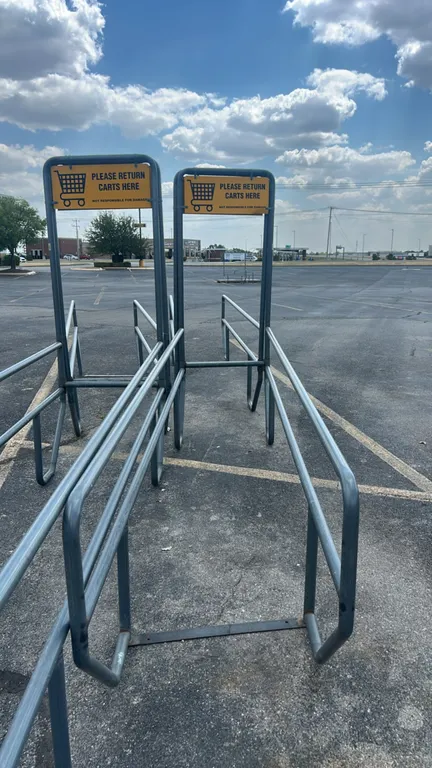 Metal shopping cart corrals. Features tubular steel construction and integrated overhead frame with yellow 'Please Return Carts Here' signage. 34"W x