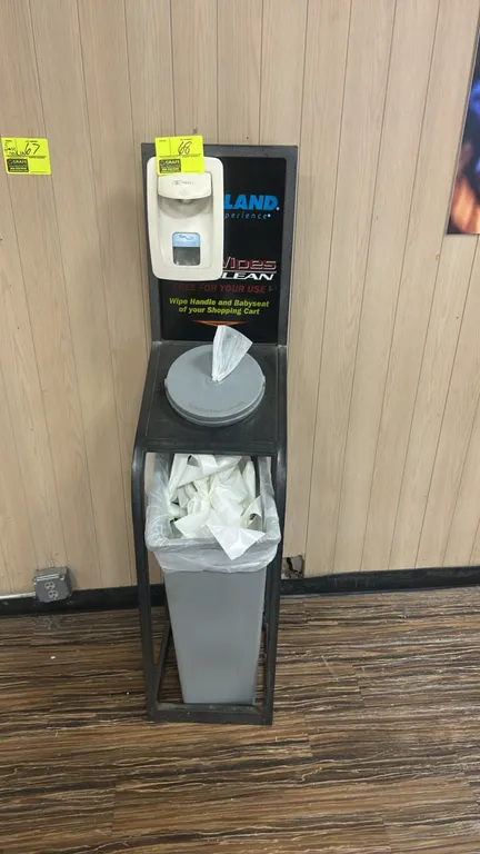 Hand sanitizer and wipe dispenser stand with poly trash bin. Features black metal frame construction, mounted Triple S FoamClean manual hand sanitizer