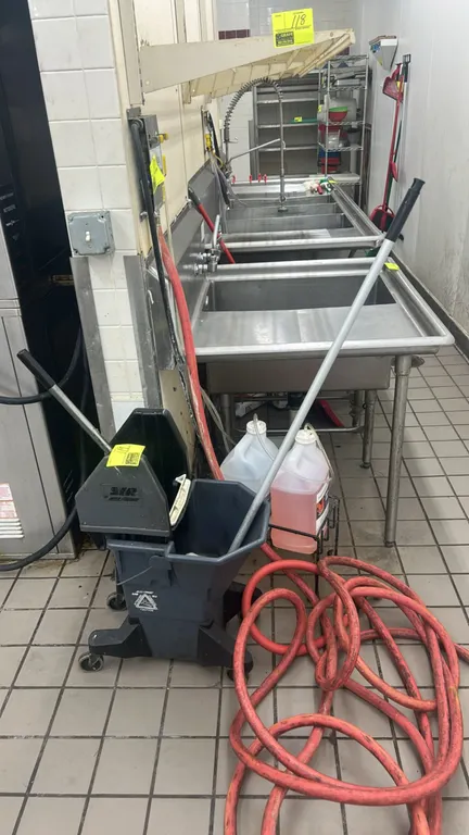 Poly mop bucket with wringer and mop. Features a side-press wringer and top carry handle. Mounted on swivel casters. Sinks, hoses, chemicals, and back