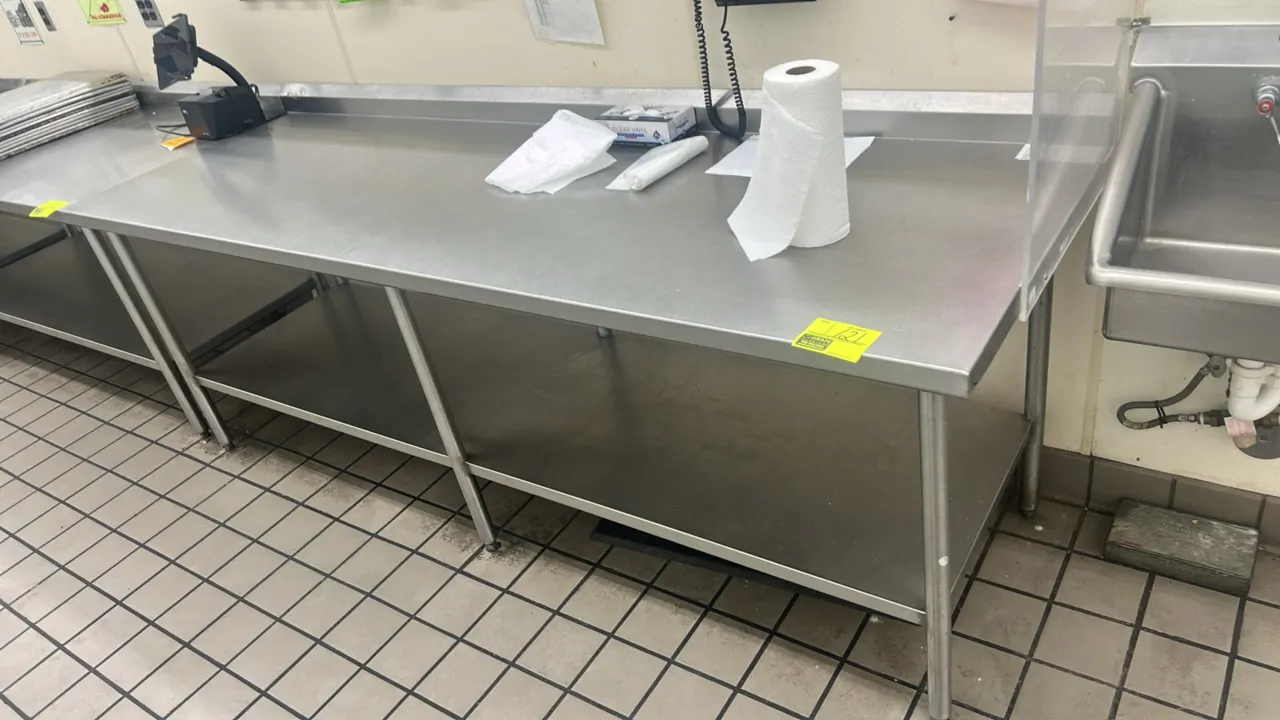 Stainless steel work table. Features a rear backsplash, lower undershelf, and tubular stainless steel legs with adjustable bullet feet. Dimensions: 96