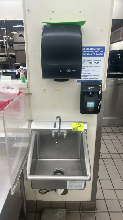 Stainless steel handwashing sink. Features gooseneck faucet with wrist-blade handles, integrated side splashes, wall-mounted Triple S paper towel disp