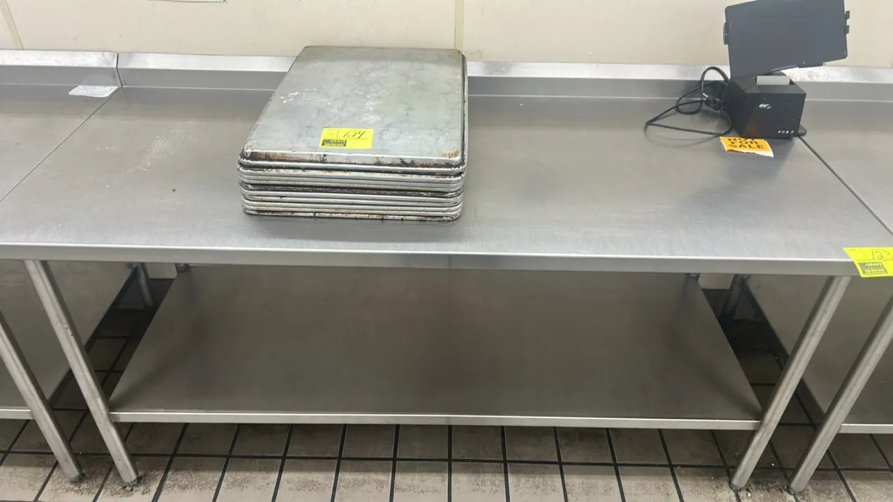 Stainless steel work table. Features a rear backsplash and undershelf. 72"L x 30"W. Mounted on tubular legs with adjustable bullet feet. Contents not