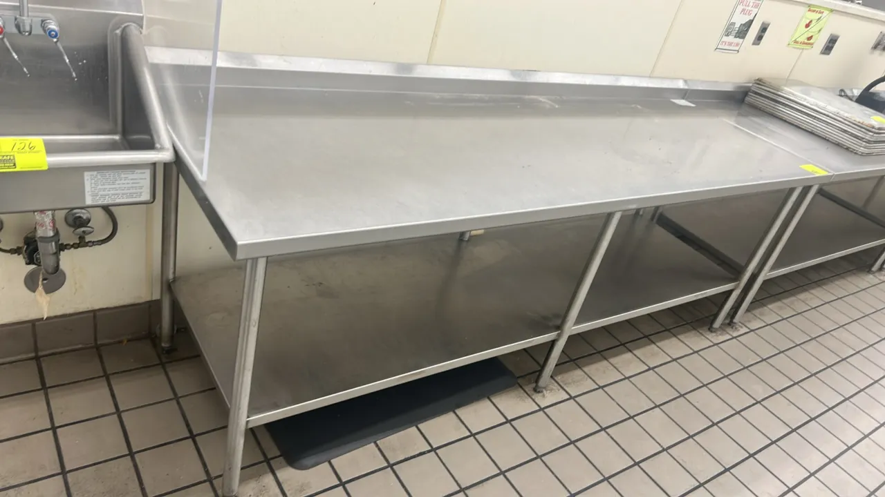 Stainless steel work table. Features a rear backsplash, full lower undershelf, and 6 tubular legs with adjustable bullet feet. 96"W x 30"D. Adjacent e