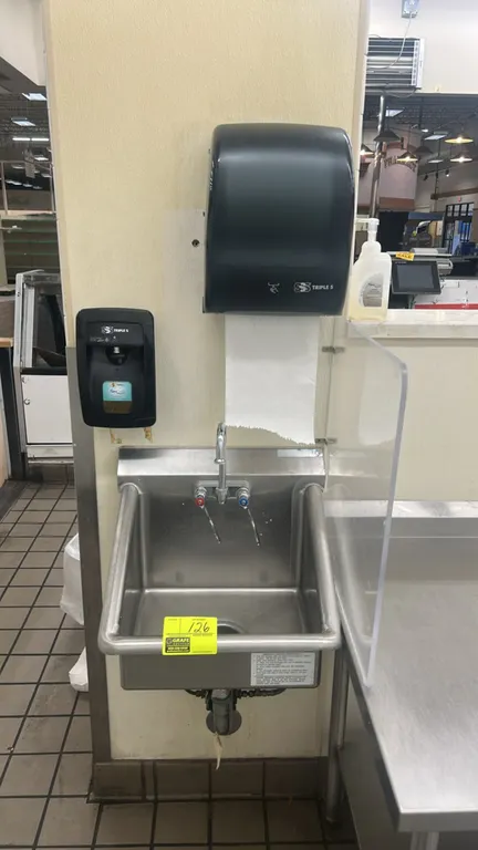 Stainless steel handwashing sink. Features a gooseneck faucet with dual wrist blade handles and a drain assembly. Includes a Triple S paper towel disp