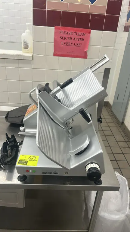 Bizerba GSP deli meat slicer. Features gravity-feed product carriage, slice thickness adjustment dial, product pusher, and detached blade sharpener as