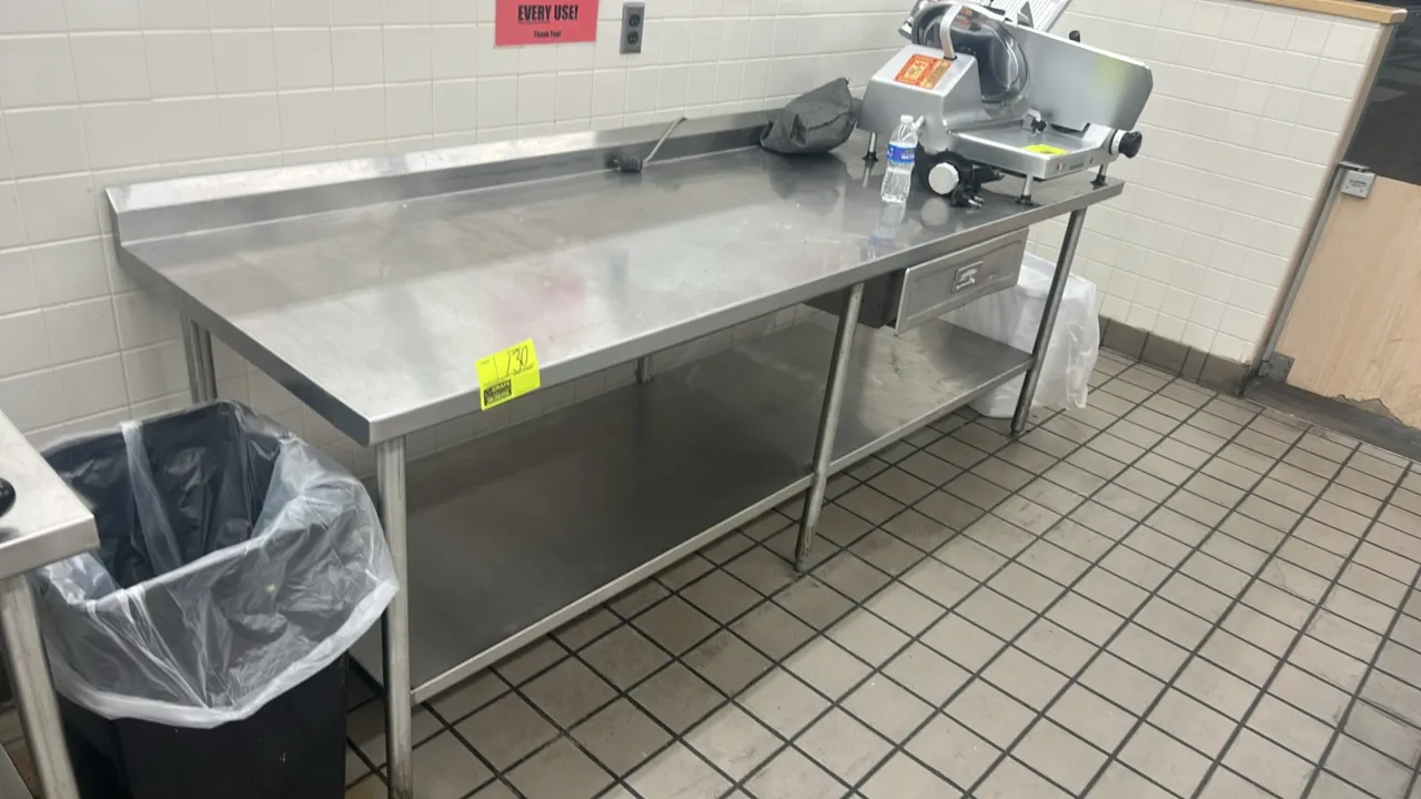 Stainless steel work table. Features a rear backsplash, stainless steel undershelf, and 1 under-counter drawer. Mounted on 6 tubular legs with adjusta