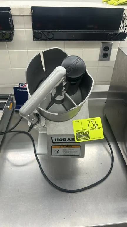 Hobart FP150-1 continuous feed food processor. Features aluminum housing, continuous feed hopper with manual pusher handle, and cylindrical feed tube.