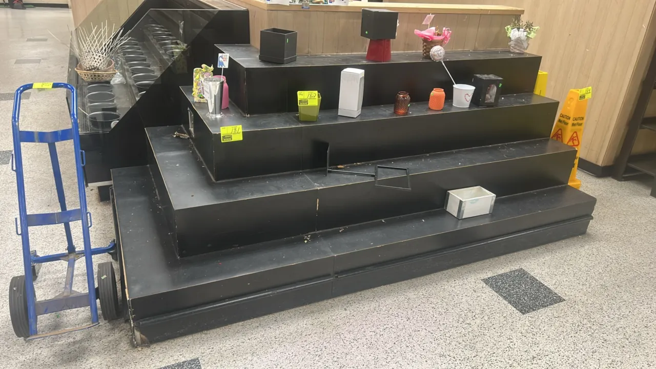 Laminate multi-tier floral display. Features a 4-tier black stepped design and integrated electrical outlet. 108" x 54". Contents not included.