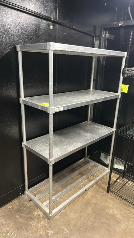 Metal 4-tier shelving rack. Features 3 solid metal shelves, 1 slotted bottom shelf, and tubular metal upright posts. Dimensions: 48"W x 20"D.