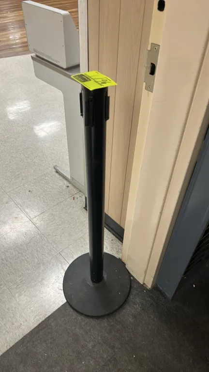Value Series retractable belt stanchion. Features a black finish post with retractable belt cassette and 4-way connector head. Mounted on a weighted c