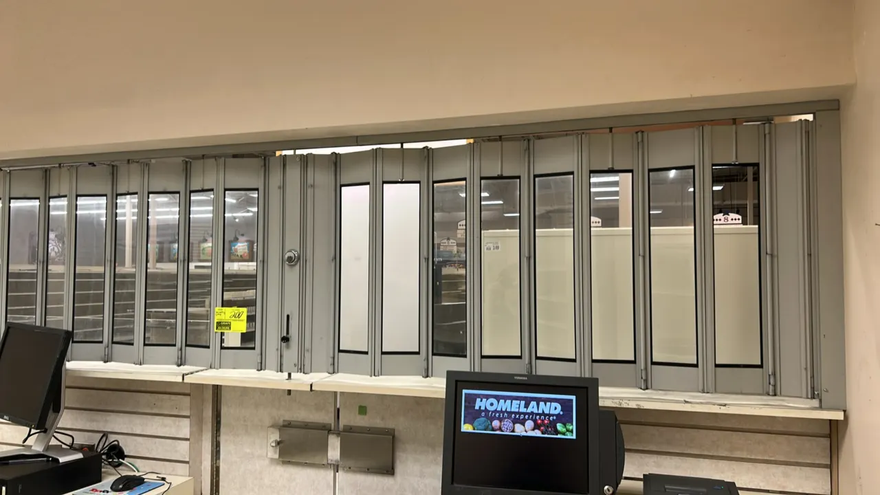 Retractable metal security gate. Features accordion folding design with clear inset panels, overhead track mount, integrated lock cylinder, and drop b