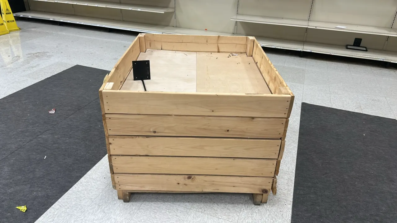 Wooden merchandising dump display bin. Features natural wood slat construction with raised perimeter rim, integrated pallet base for forklift or palle