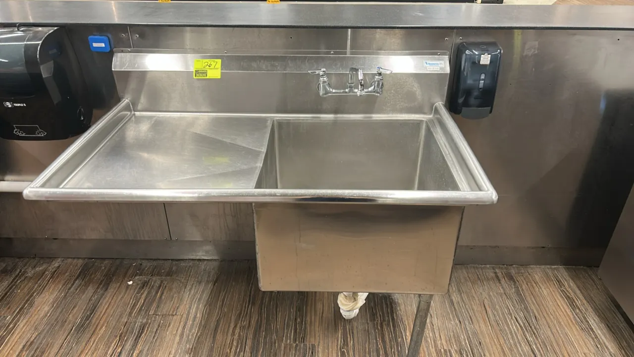Stainless steel single-compartment sink. Features a left-hand drainboard, backsplash, splash-mount faucet, and wall-mount soap dispenser. Dimensions: