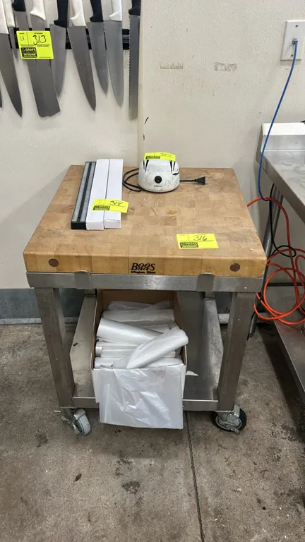 John Boos portable work table. Features wood butcher block top, stainless steel frame, and lower undershelf. 2'L. Mounted on casters. Contents not inc