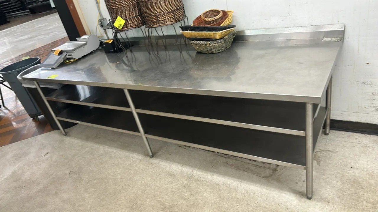 Stainless steel work table. Features a rear backsplash, 2-tier undershelf, and stainless steel tubular legs with adjustable bullet feet. Dimensions: 1