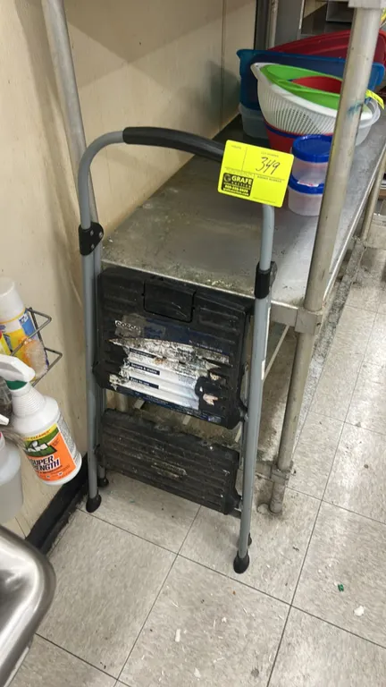 Cosco 2-step folding step ladder. Features tubular metal frame, textured plastic steps, and top hand grip.
