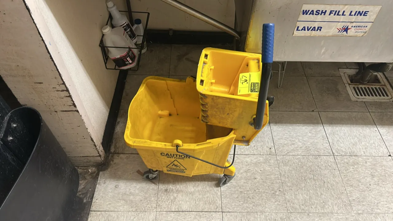 Polyethylene mop bucket with wringer. Features yellow molded plastic body with 'Caution Wet Floor' graphics, wringer with lever handle, and metal bail