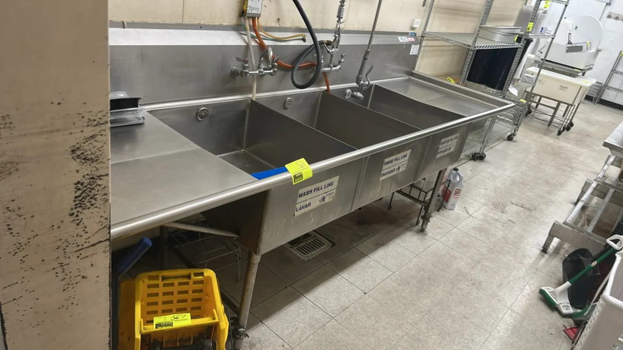 Stainless steel 3-compartment sink. Features left and right drainboards, integrated backsplash, pre-rinse spray assembly, and wall-mount faucets. 10'