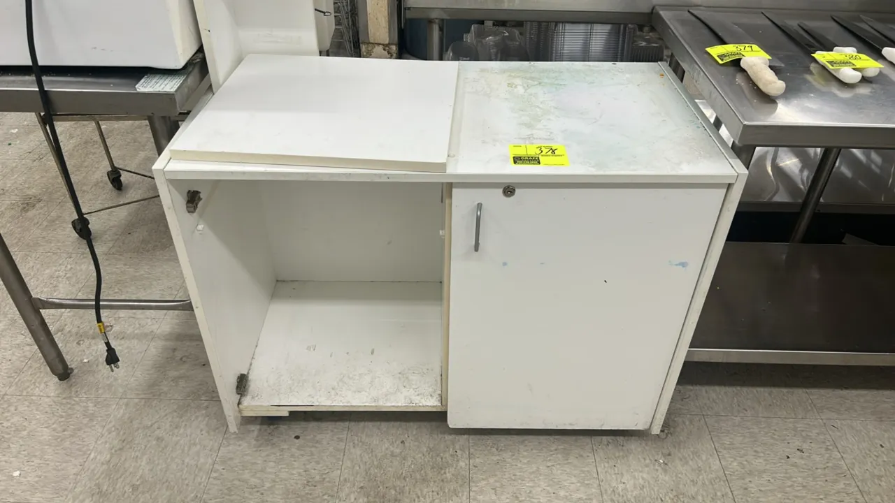 White laminate storage cabinet. Features a single hinged cabinet door with handle on the right and an open storage compartment on the left. Dimensions