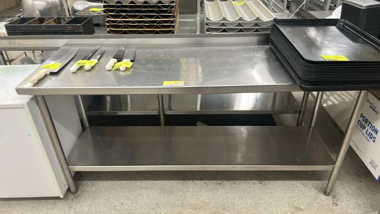Stainless steel work table. Features a lower undershelf and rear backsplash. Supported by tubular legs with adjustable bullet feet. 6' x 2'. Contents
