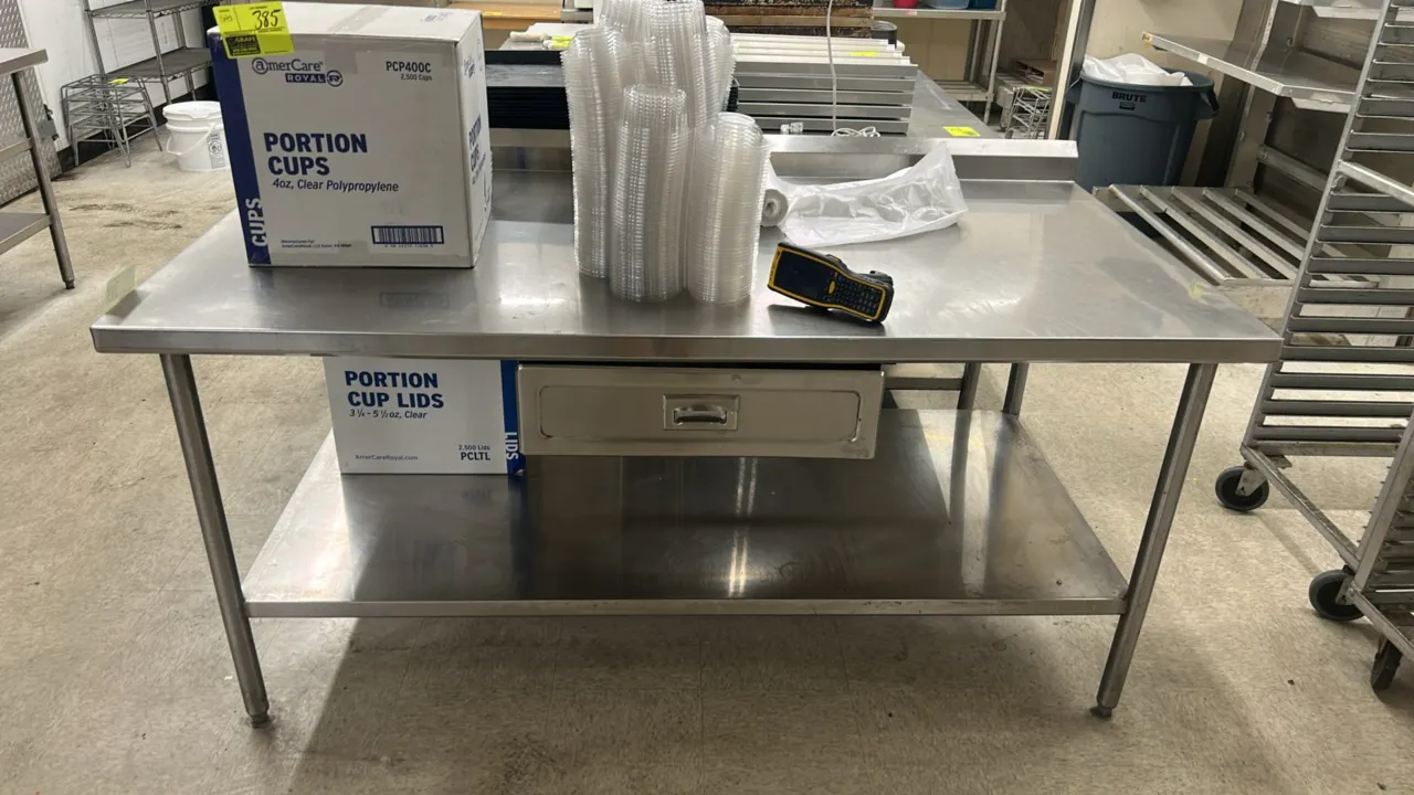 Stainless steel work table. Features a rear backsplash, lower undershelf, and single pull-out drawer. 6'L x 3'W. Mounted on tubular legs with adjustab